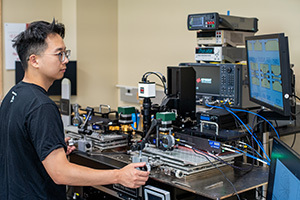 A student operates advanced lab equipment with multiple screens, one displaying circuit diagrams.