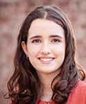 Smiling young woman with long dark hair, wearing a coral-colored shirt.